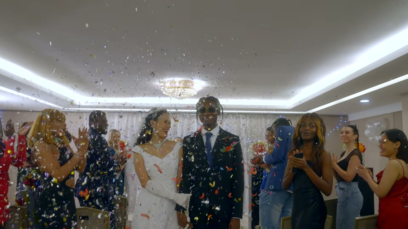 A bride and groom walking through falling confetti as guests clap on either side