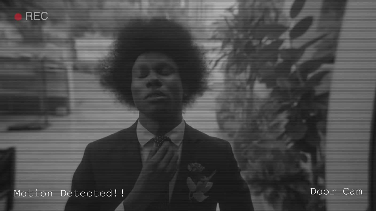 Black-and-white door camera footage of a young man in a suit outside a door, with a Motion Detected alert
