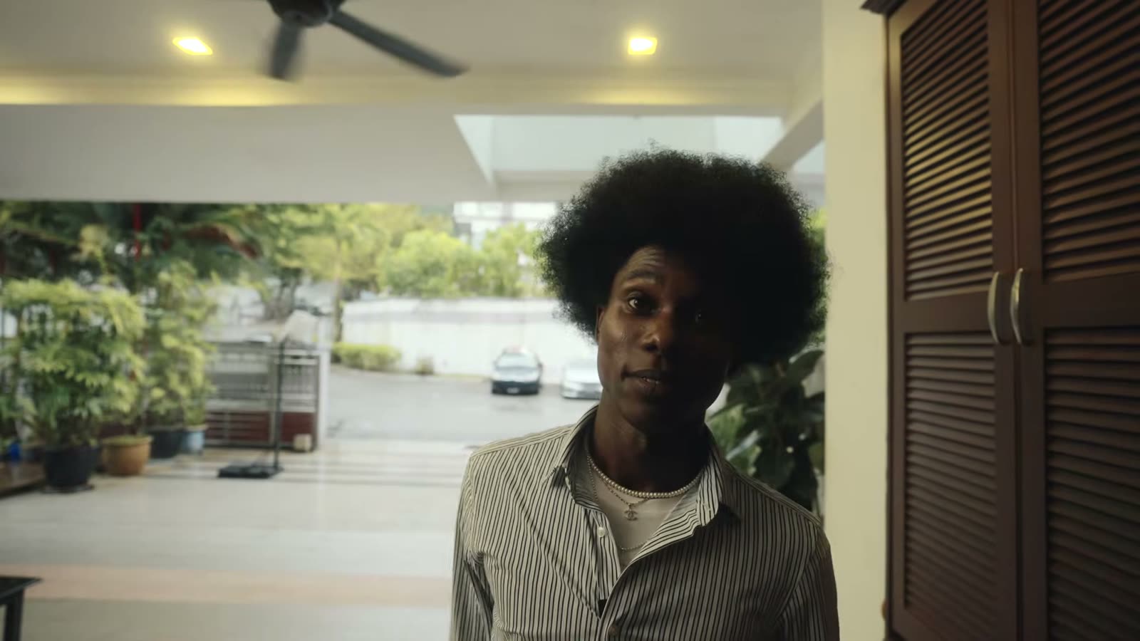 The same young man back at the doorway, now in a casual striped shirt