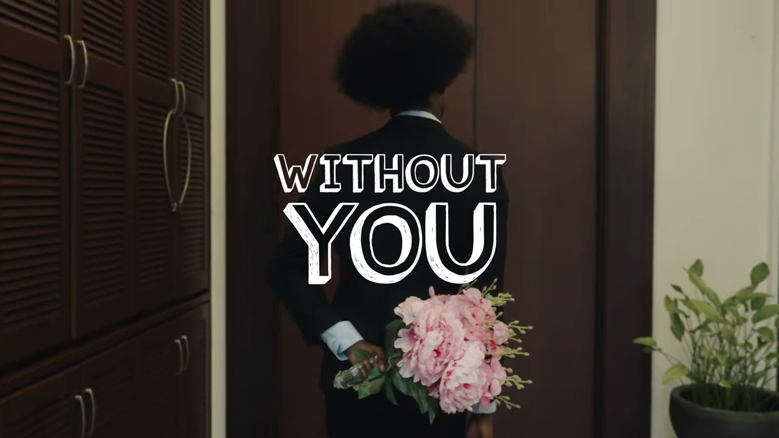 The title card of the Without You music video: a young man at a door with pink flowers behind his back